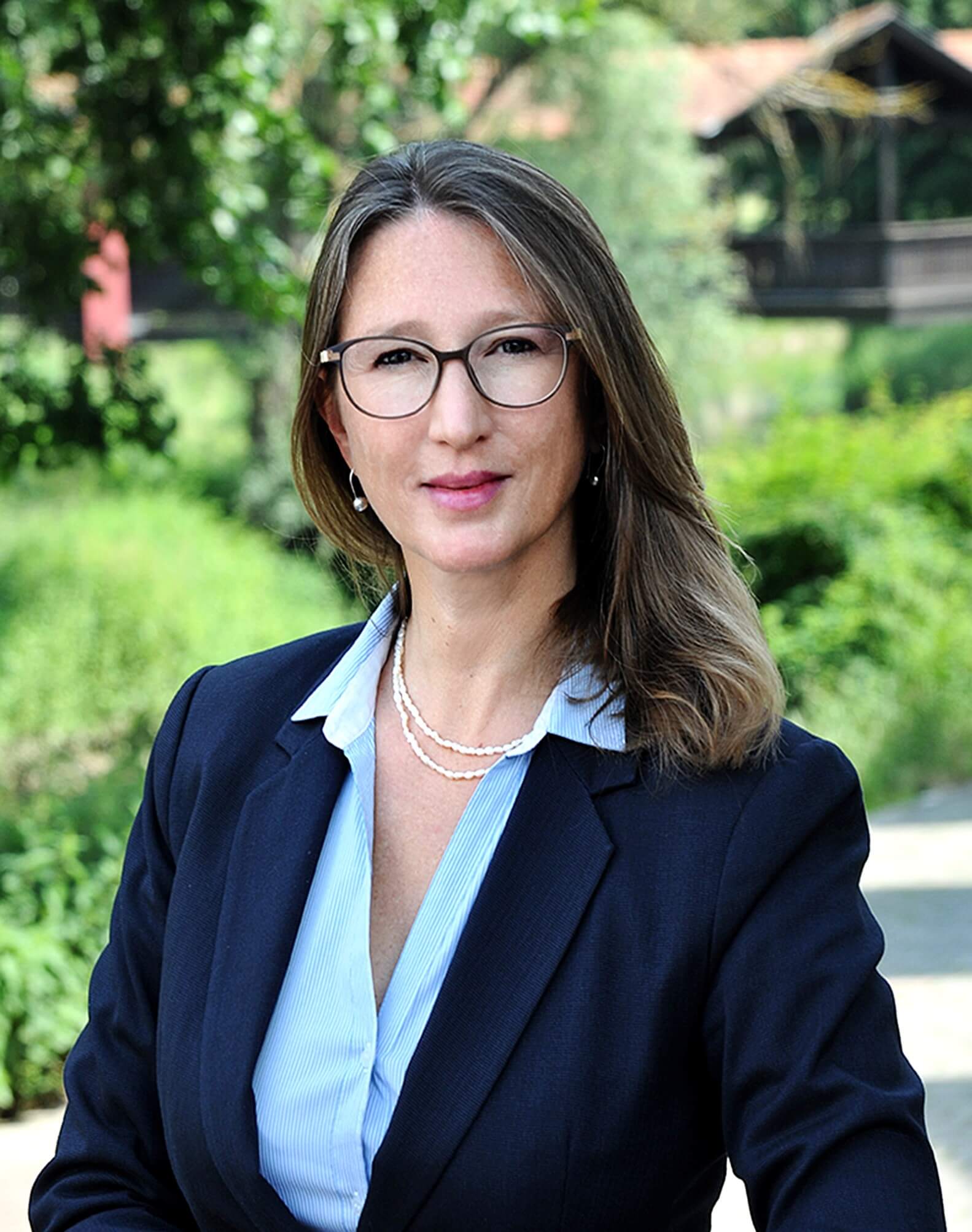anja-nina-kramer Portrait Anja Nina Kramer in hellblaue Bluse und dunklem Blazer vor parkähnlichem Hintergrund
